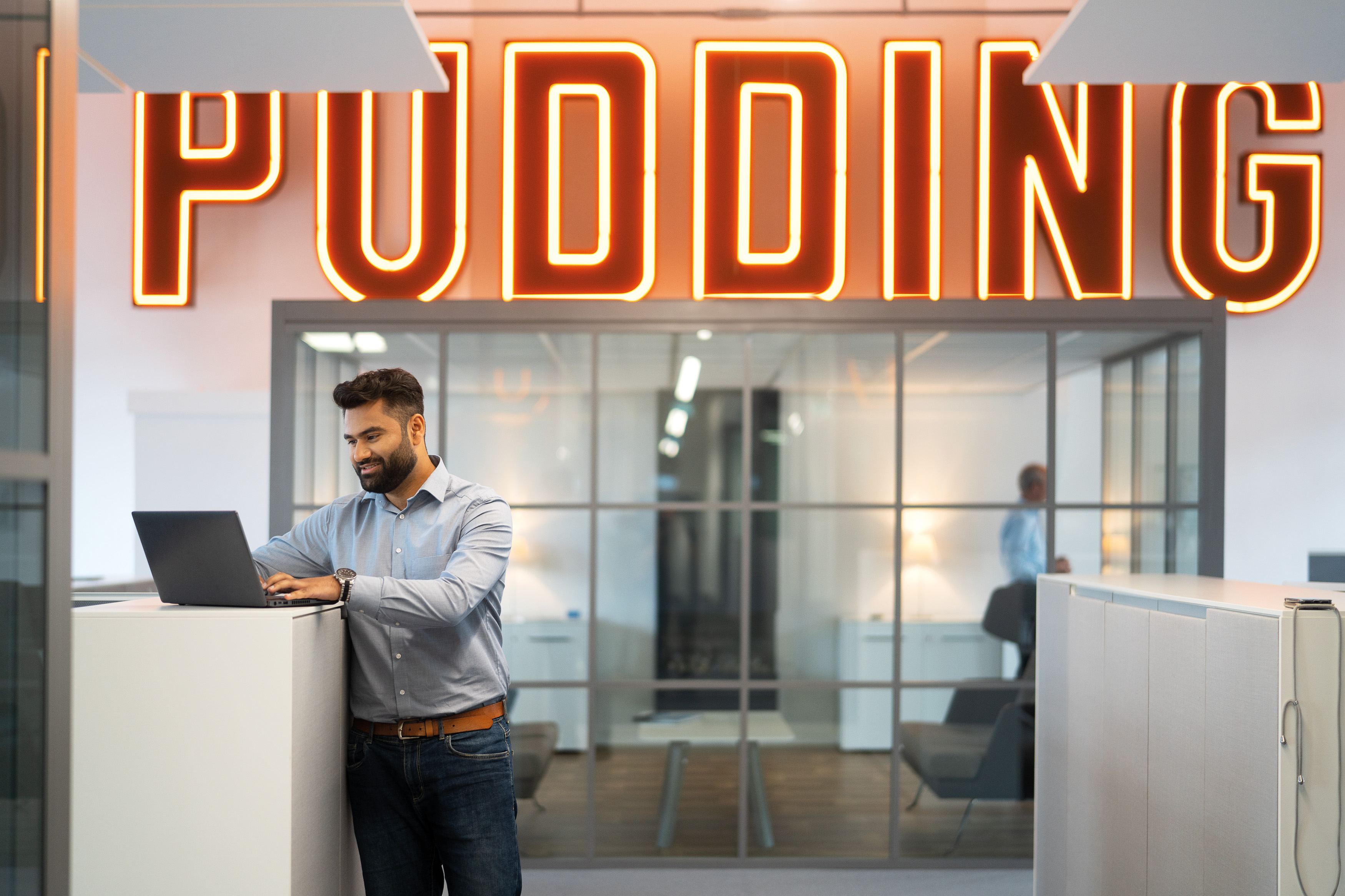 Mann arbeitet an einem Stehtisch. hinter ihm sieht man einen großen Schriftzug "Pudding"